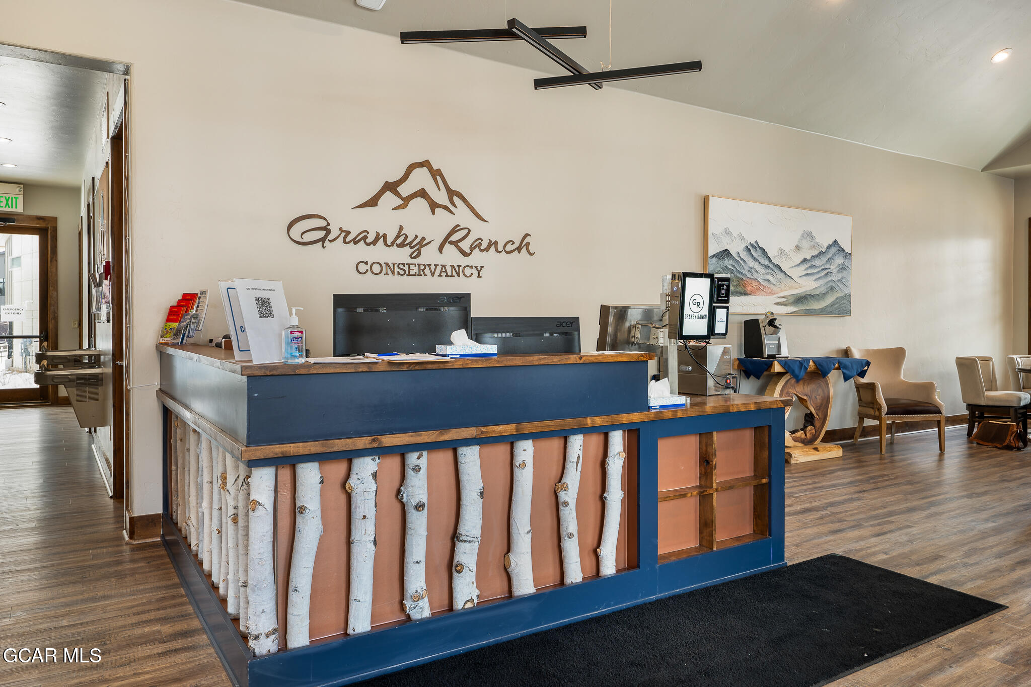 Reception lobby with a blue desk, birch-log trim, and Granby Ranch Conservancy sign.