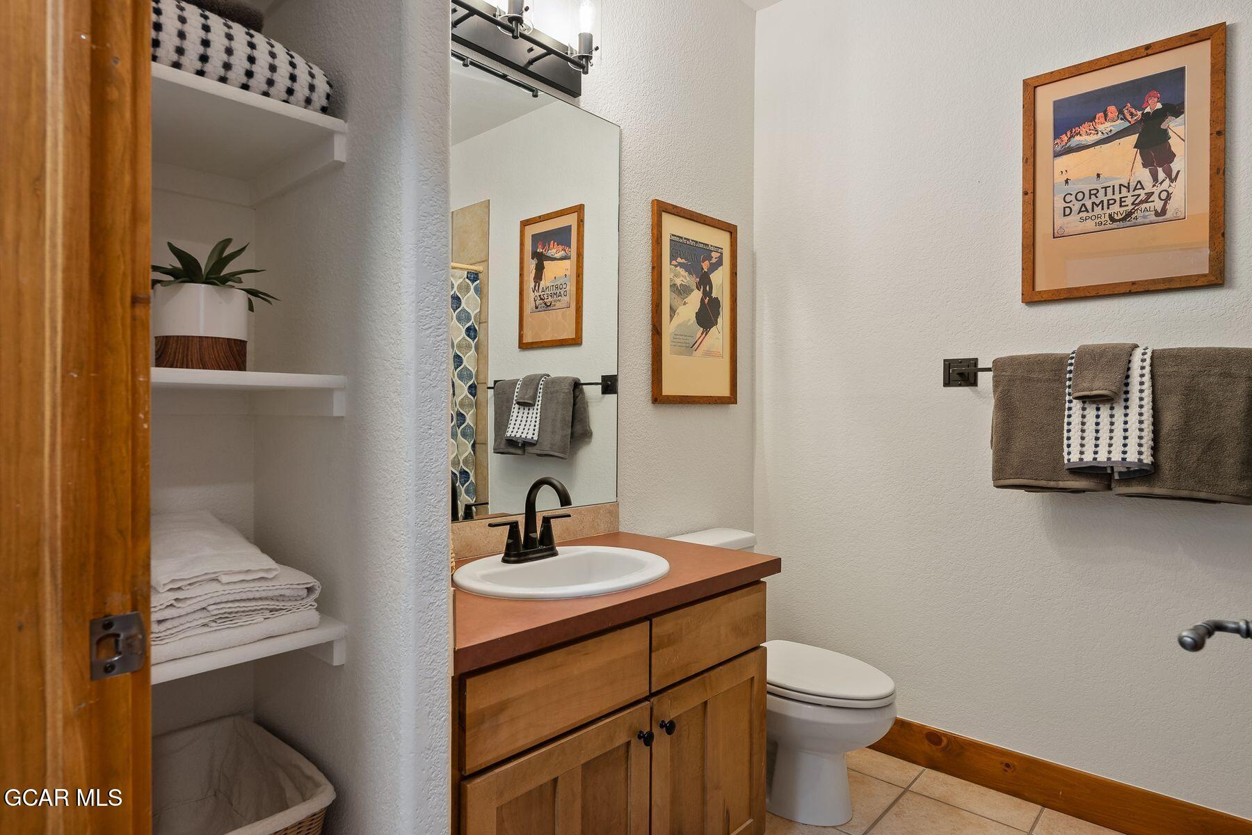 Bathroom with a wood vanity, white sink, open towel shelves, and vintage ski posters.