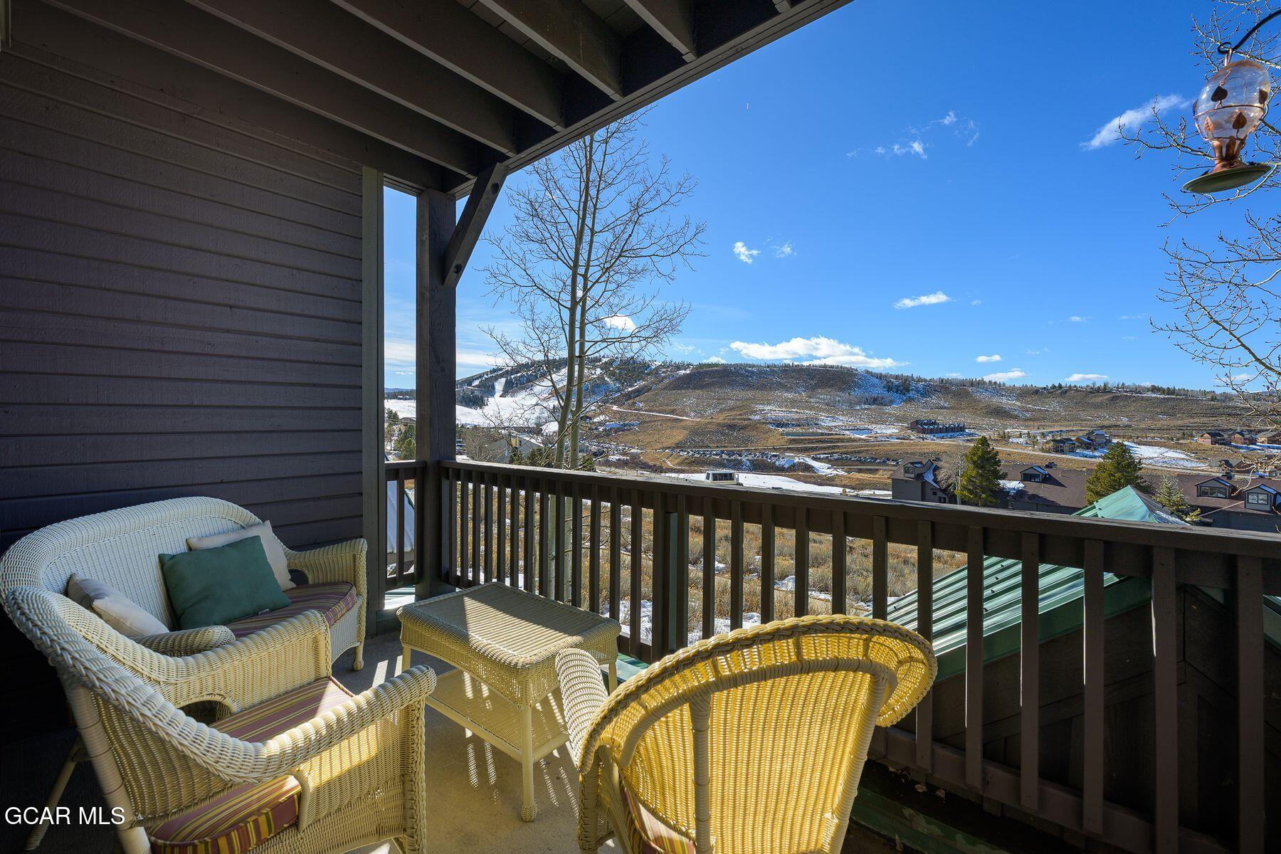 Covered balcony with wicker seating overlooking a snow-dusted hillside and nearby homes.