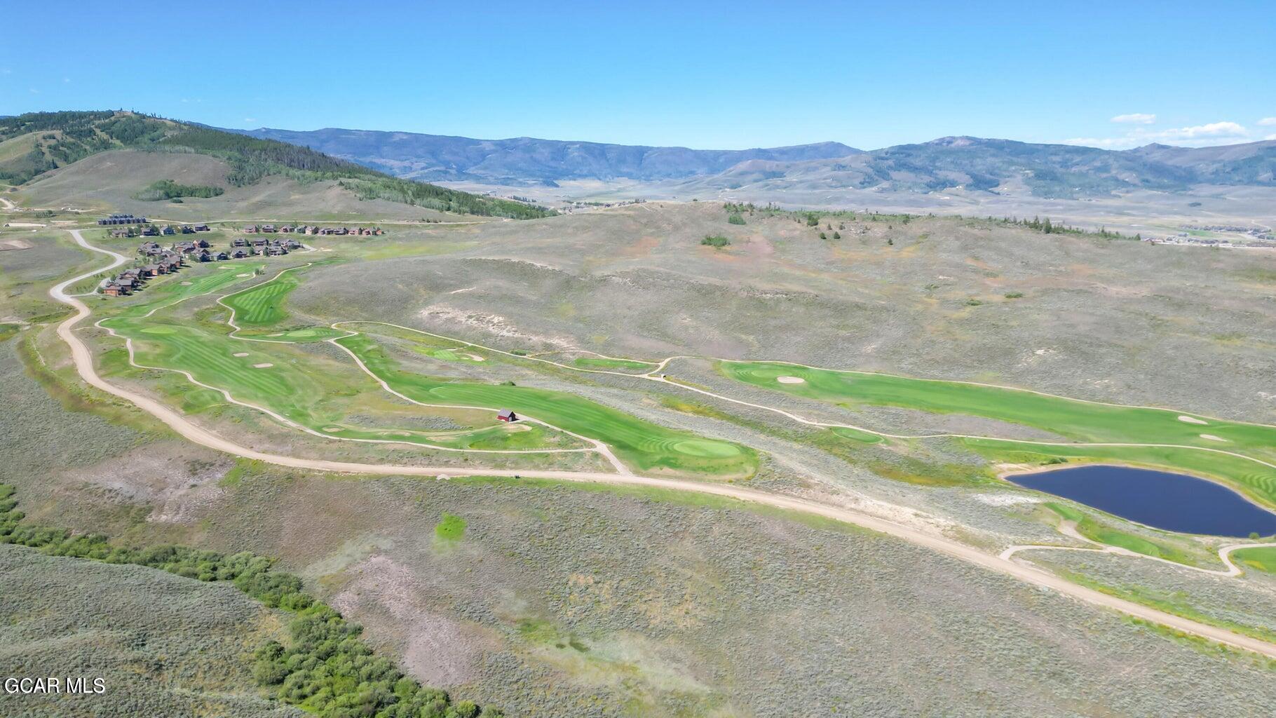Aerial view of a mountain golf course with clustered homes, winding fairways, and a pond.