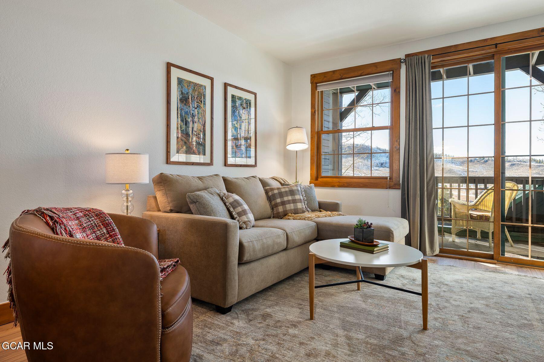 Furnished living room with a beige sectional, leather chair, and balcony windows overlooking snow-dusted hills.