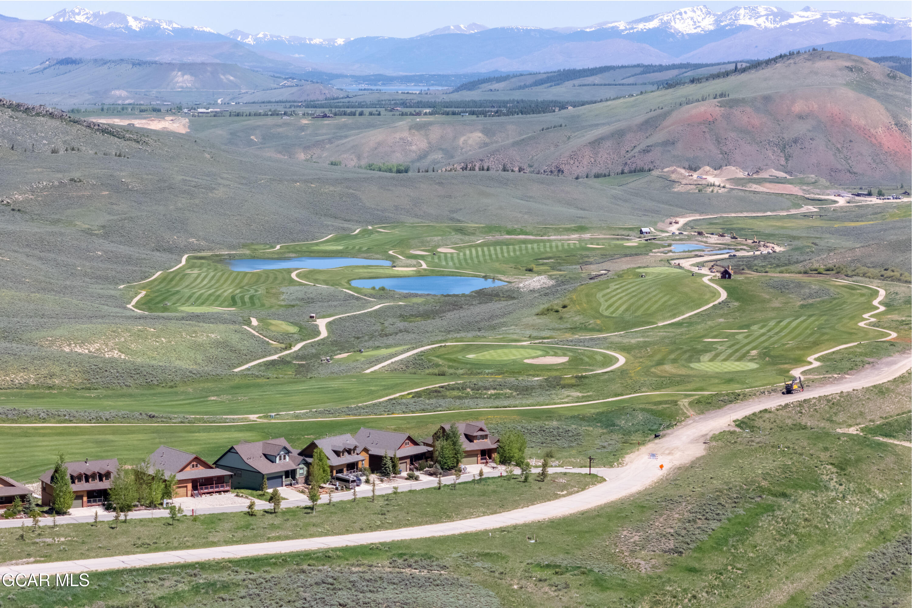 Aerial view of a golf course community with ponds, homes, and snow-capped mountains.