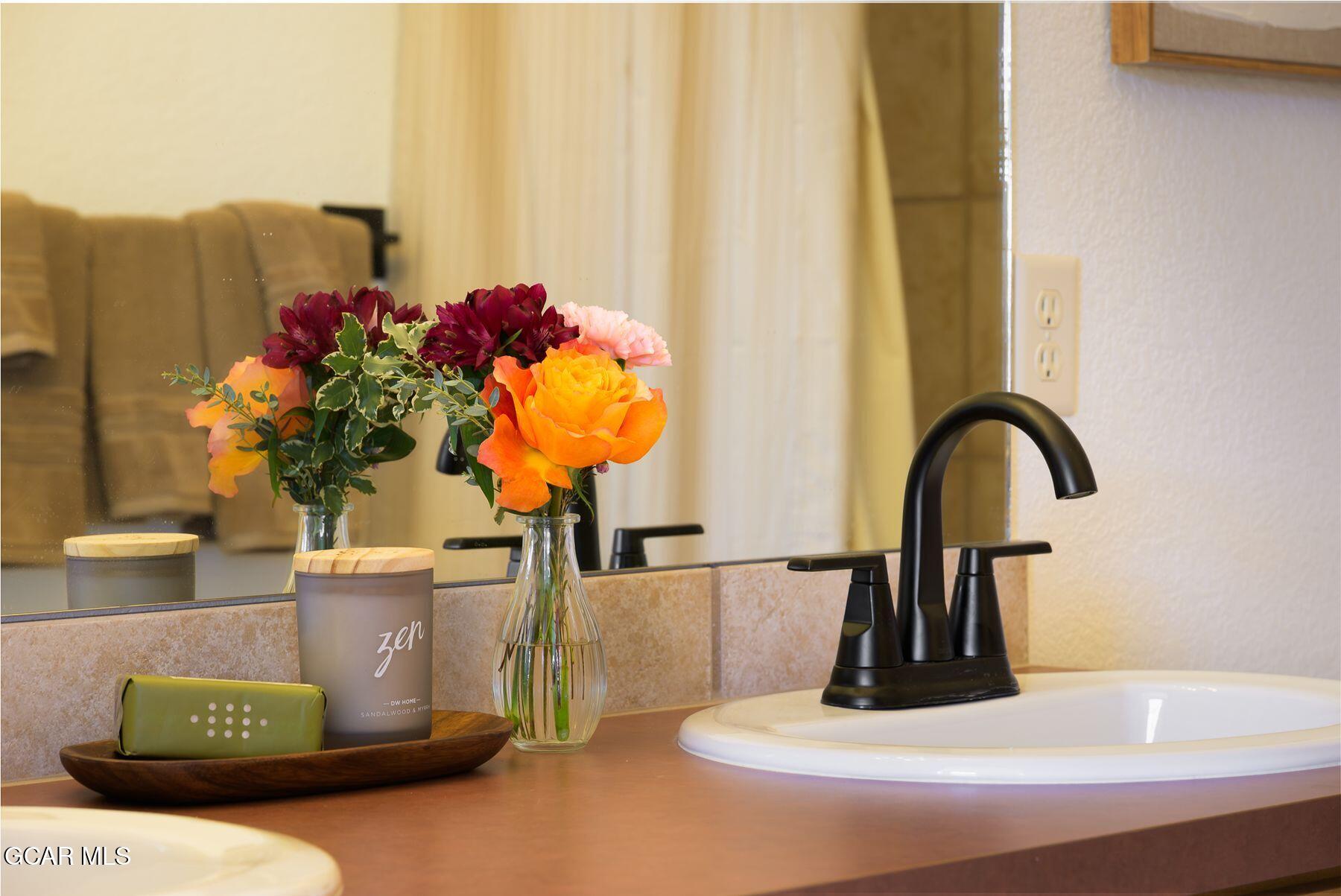 Bathroom vanity with a black faucet, white sink, and colorful flowers on the counter.