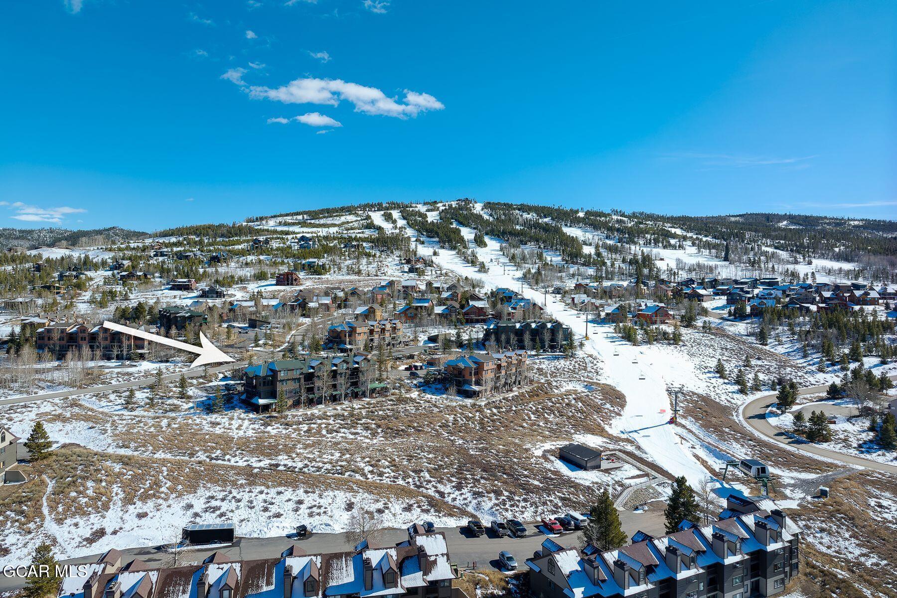 Aerial view of a mountain community and ski slope, with an arrow pointing to a foreground building.