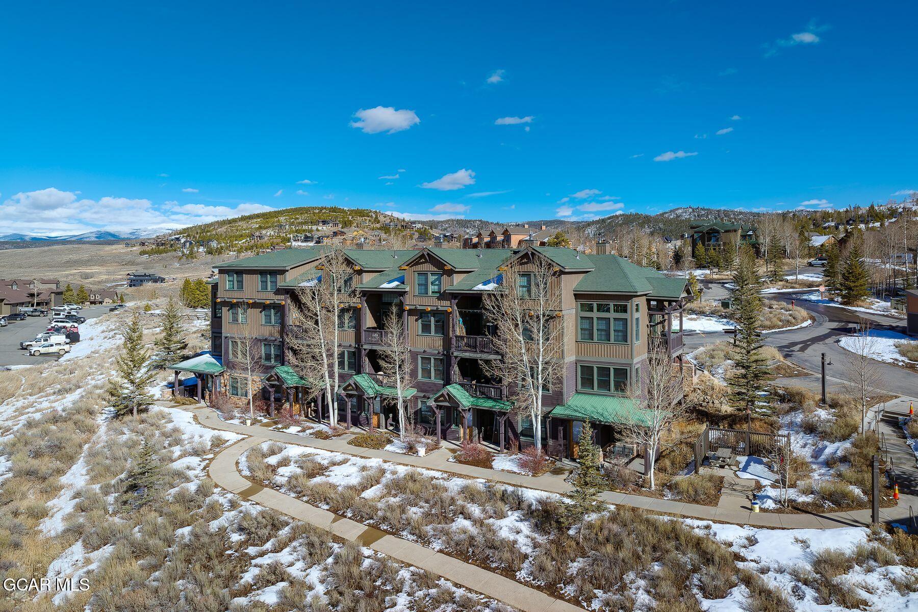 Multi-unit building with green roofs and balconies amid snow-dusted grounds and mountain hills.
