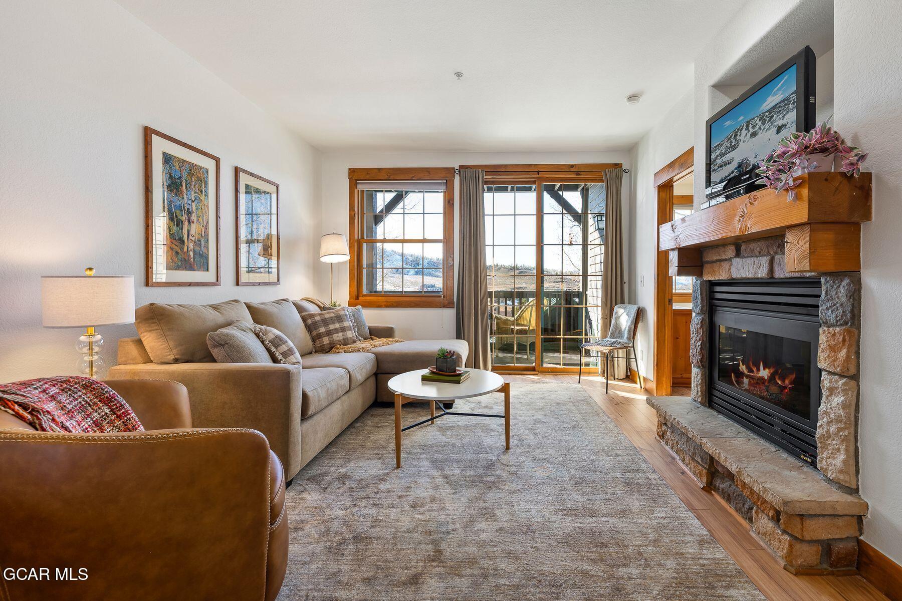 Living room with a stone fireplace, beige sectional, and balcony windows overlooking a snowy landscape.