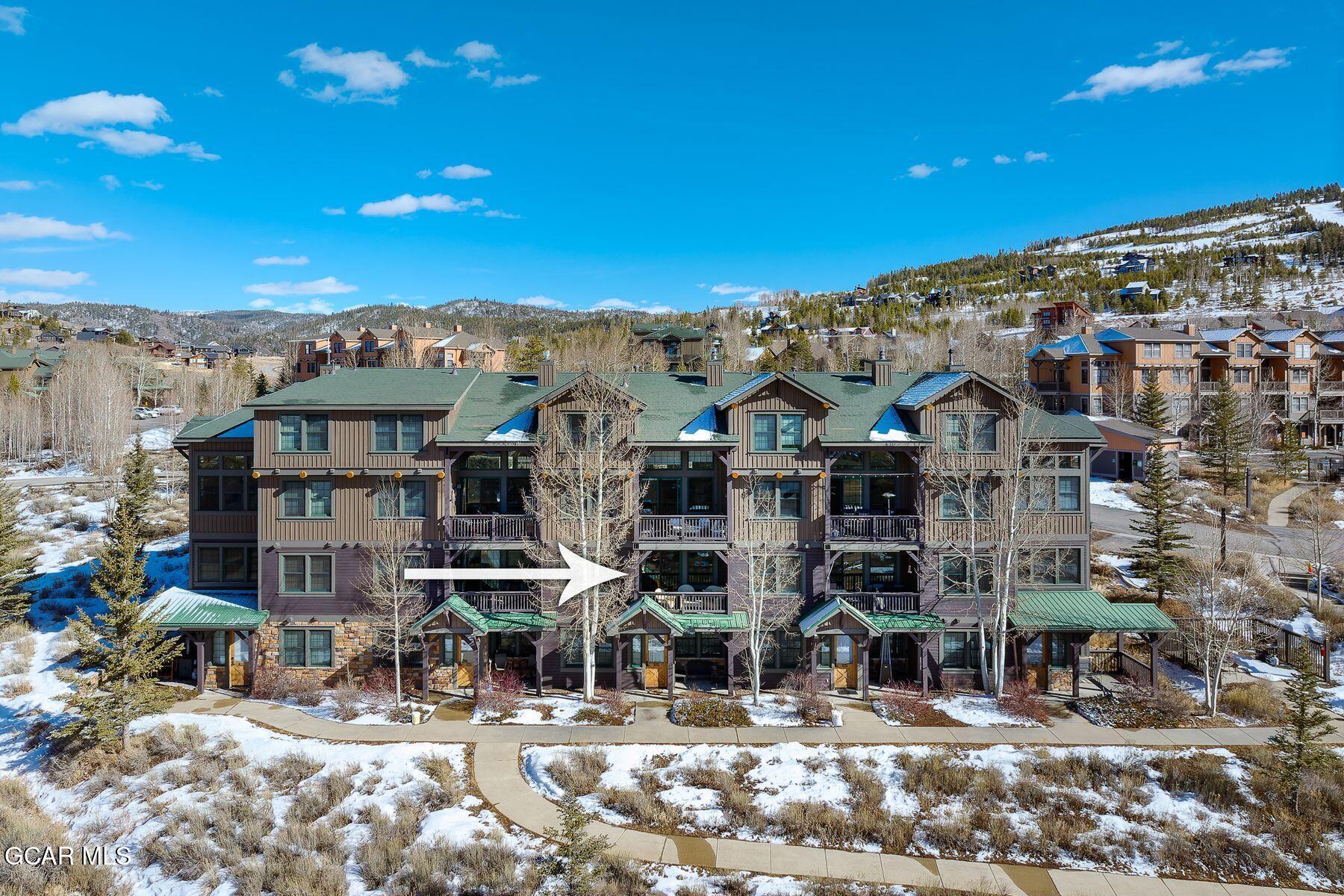 Condominium building with a white arrow pointing to a unit, surrounded by snow-covered grounds and hills.