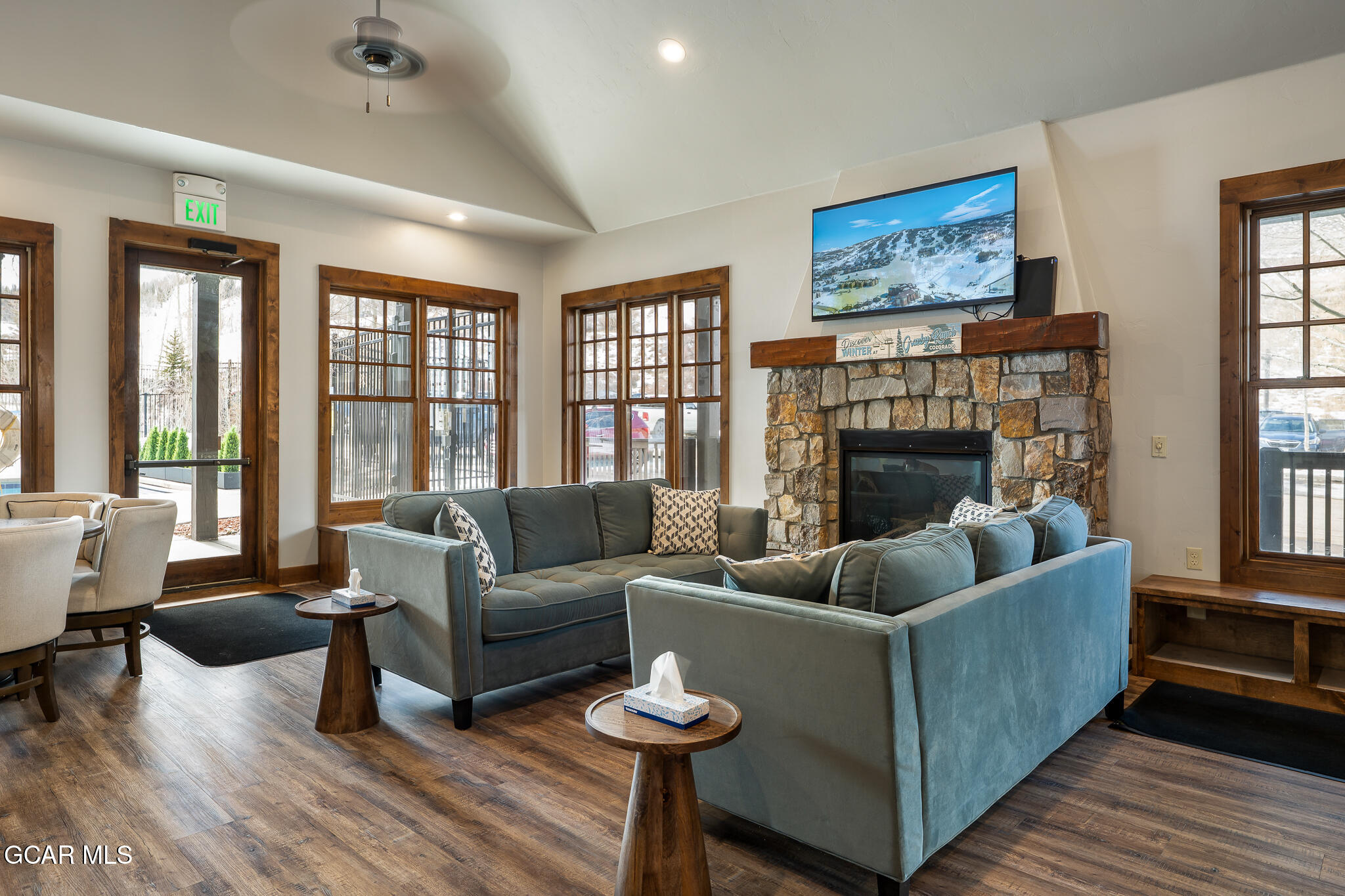 Furnished living room with blue-gray sofas facing a stone fireplace beneath a mounted television.