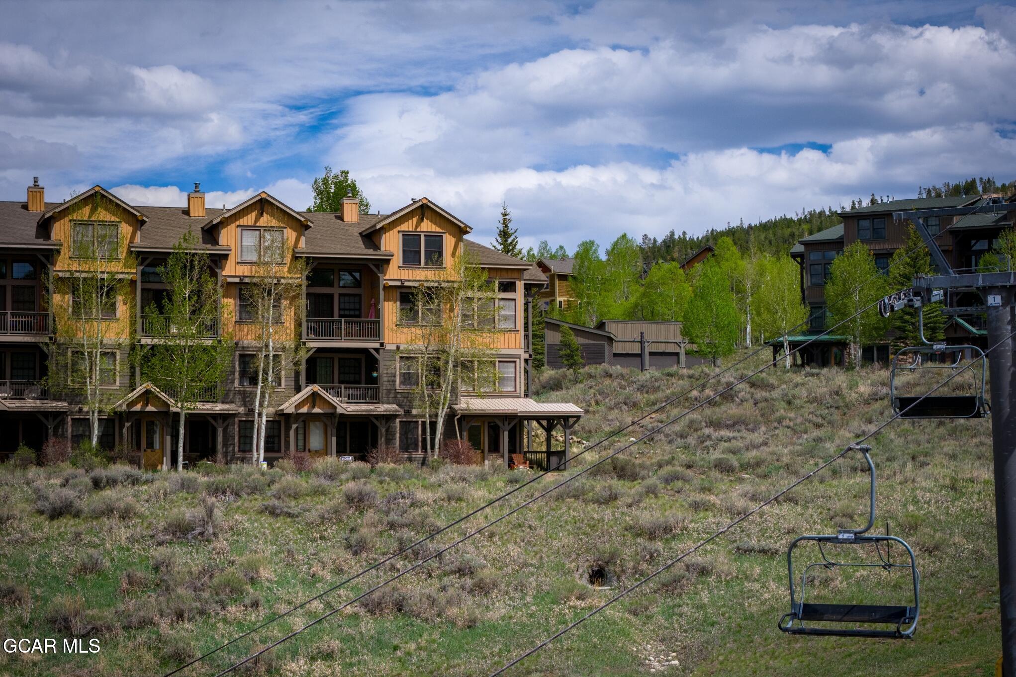 Condominium buildings beside an empty ski lift on a grassy slope.