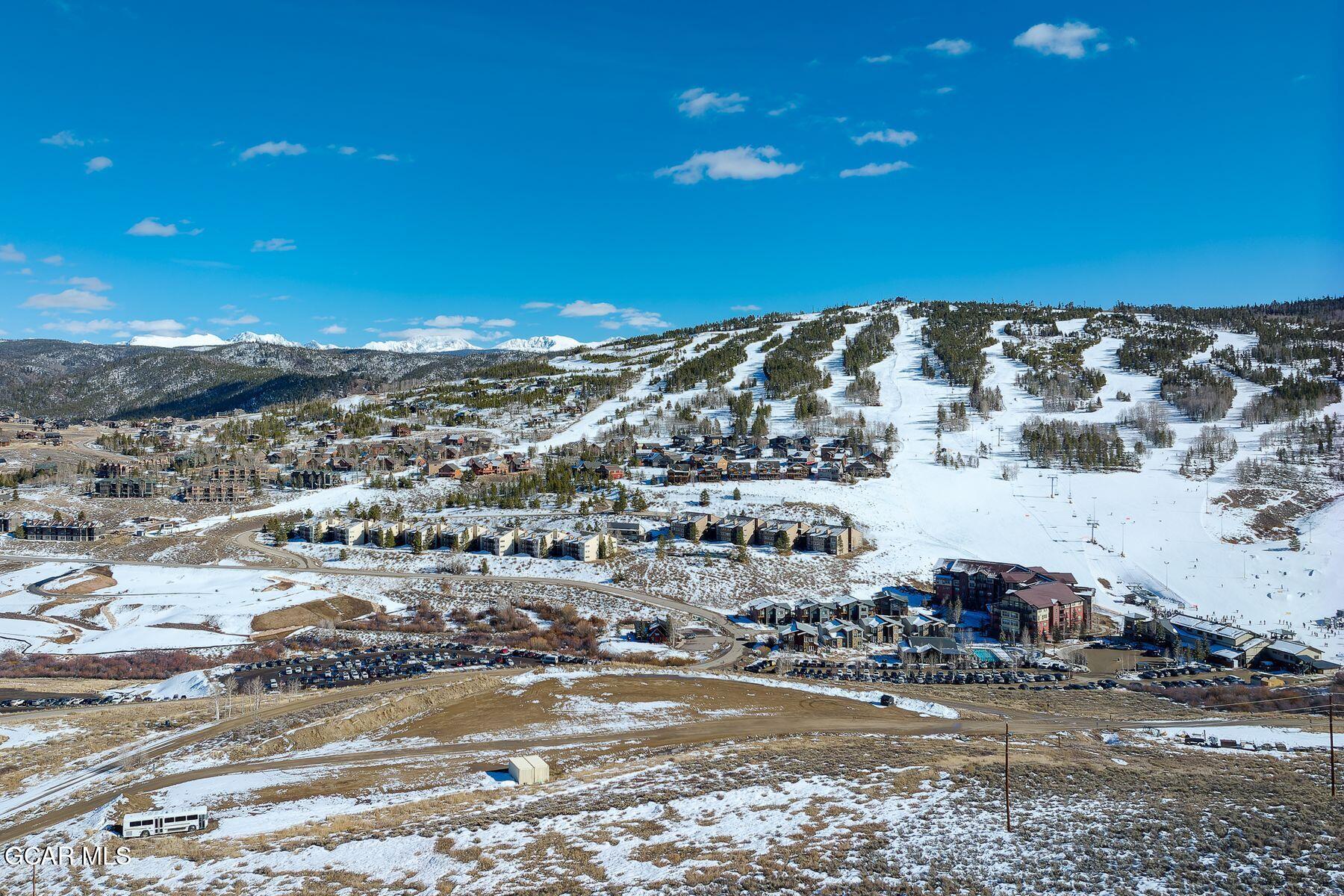 Panoramic view of snowy ski runs, resort buildings, and distant mountain peaks.