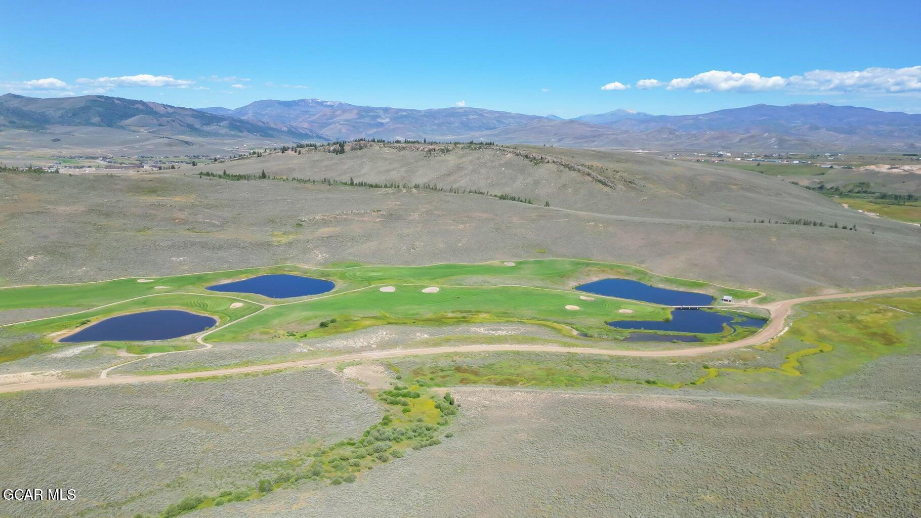 Aerial view of a golf course with ponds and mountain ranges in the distance.