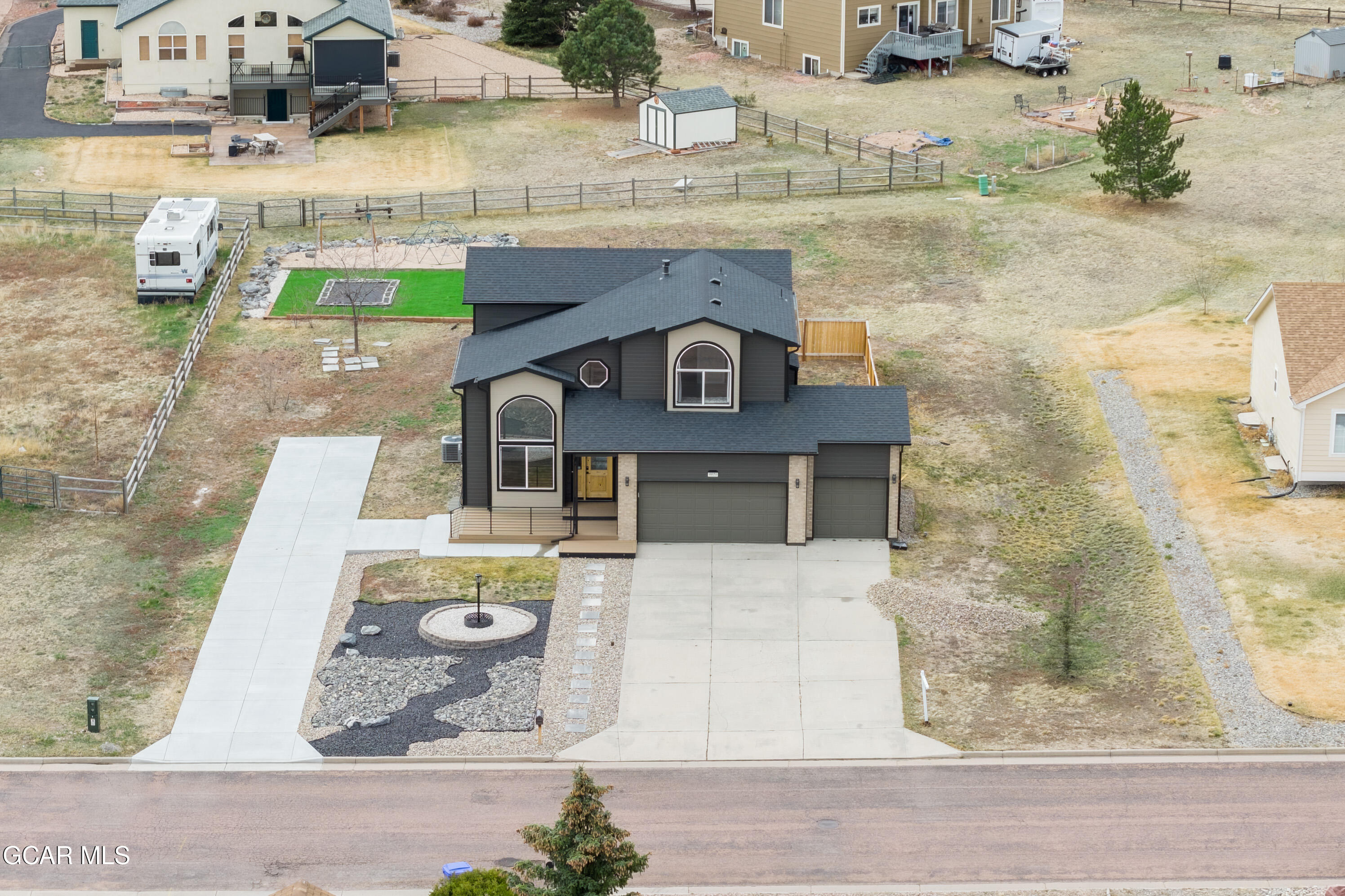 Aerial view of a two-story home with a wide driveway and landscaped yard with a circular fire pit.
