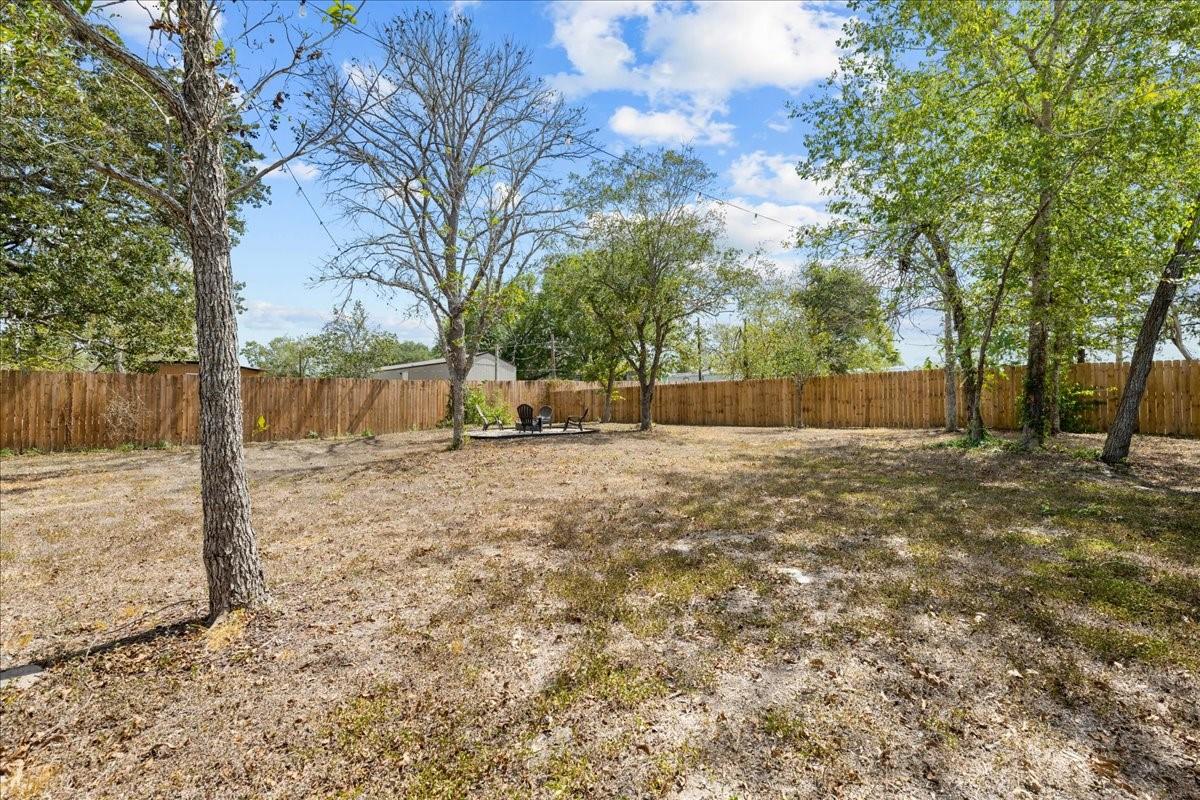 Fenced backyard with mature trees and a small seating area.