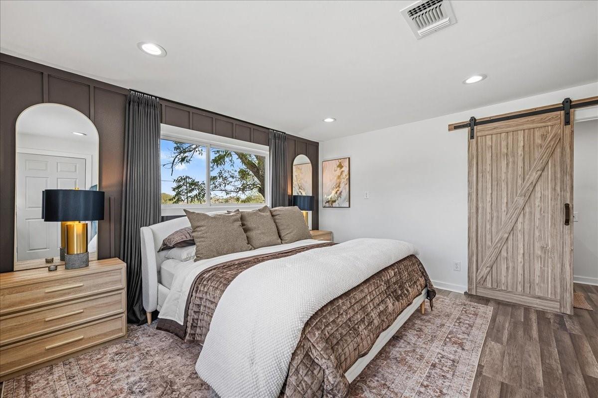 Staged bedroom with a large bed, rustic sliding barn door, and dark paneled accent wall.