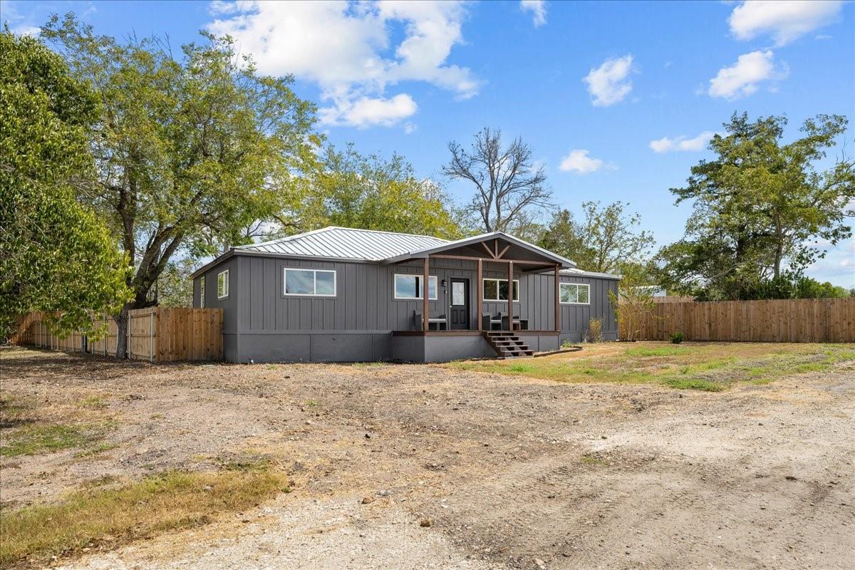 Gray single-story home with a covered porch, metal roof, and fenced yard.