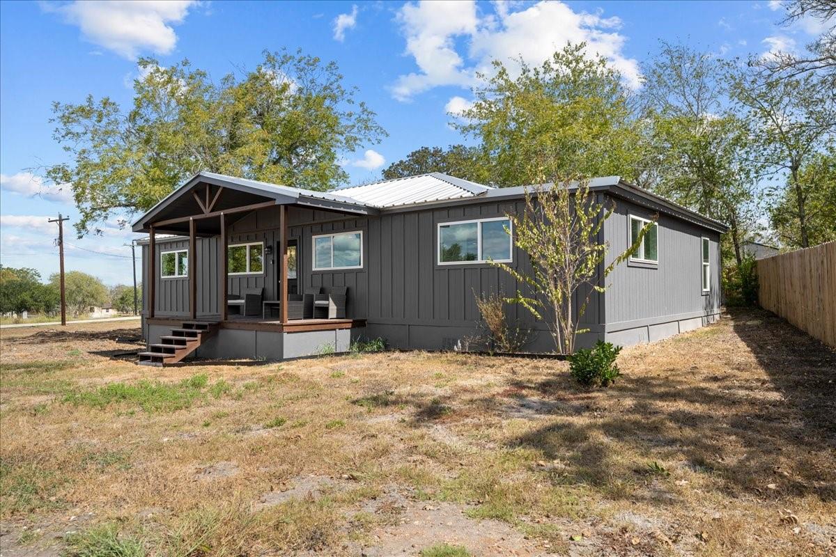 Single-story dark gray home with a covered porch, metal roof, and dry yard.