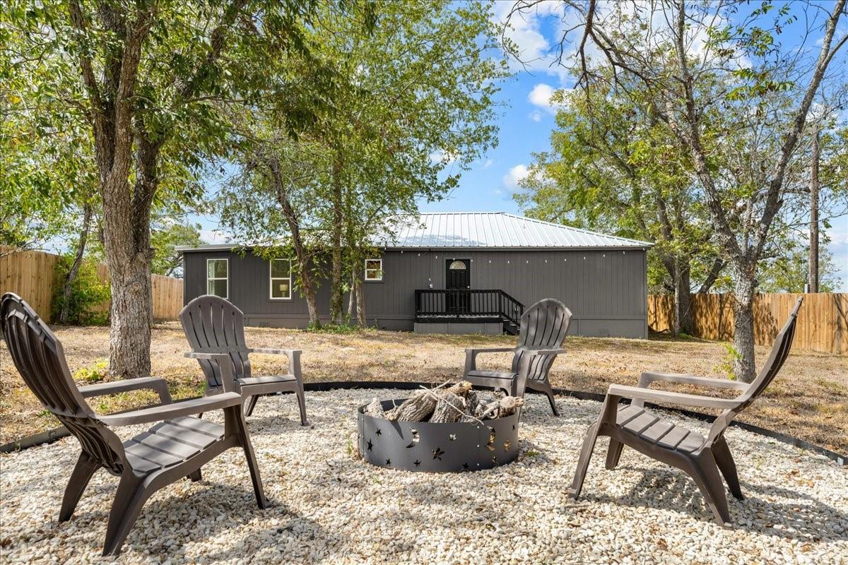 Dark gray single-story home behind a gravel yard with Adirondack chairs and a fire pit.