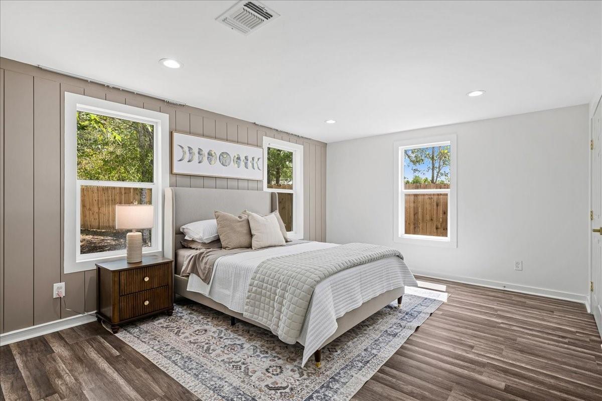 Staged bedroom with a bed against taupe paneling, three windows, and a patterned rug.