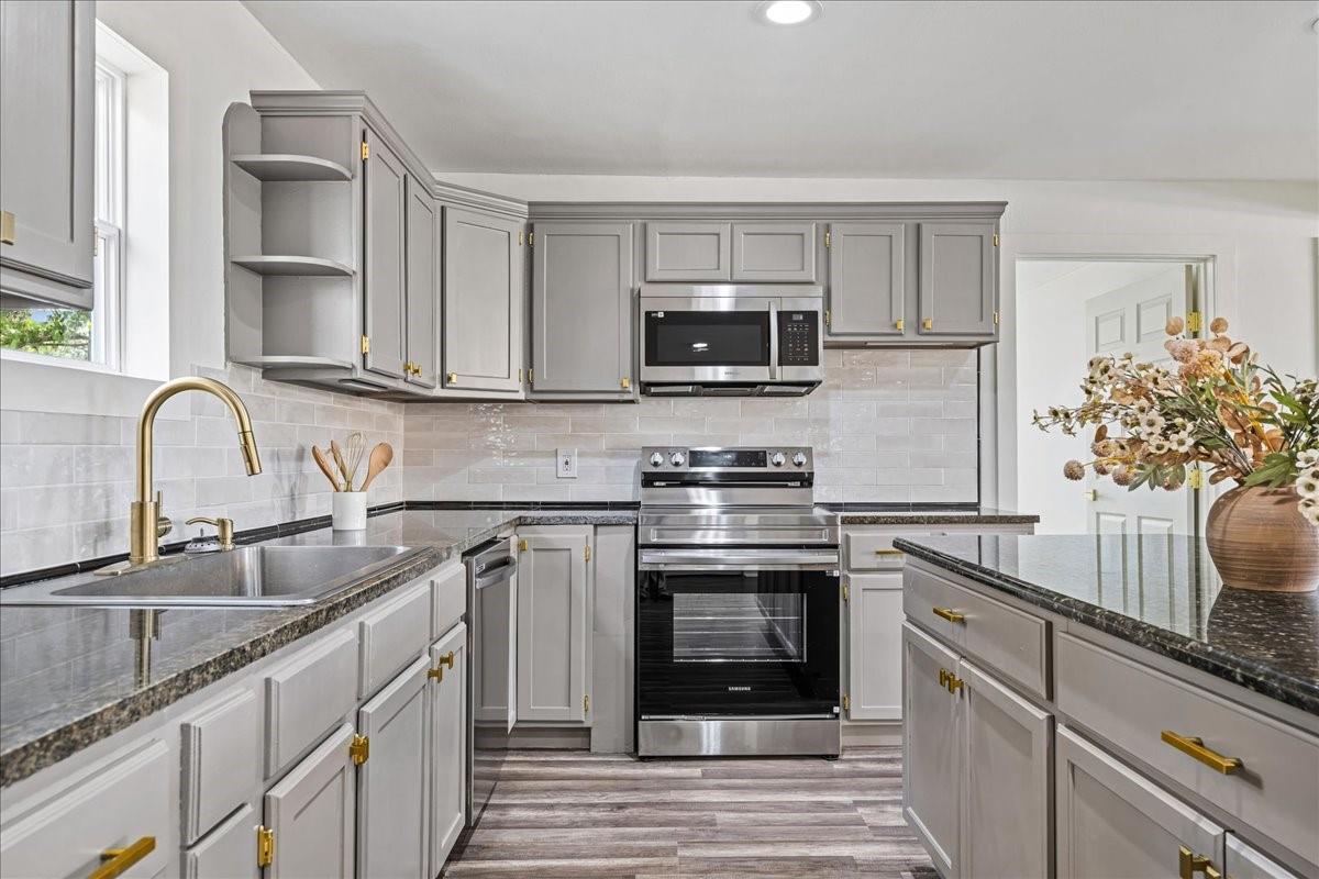 Kitchen with gray cabinets, stainless steel appliances, dark countertops, and a flower arrangement on the island.