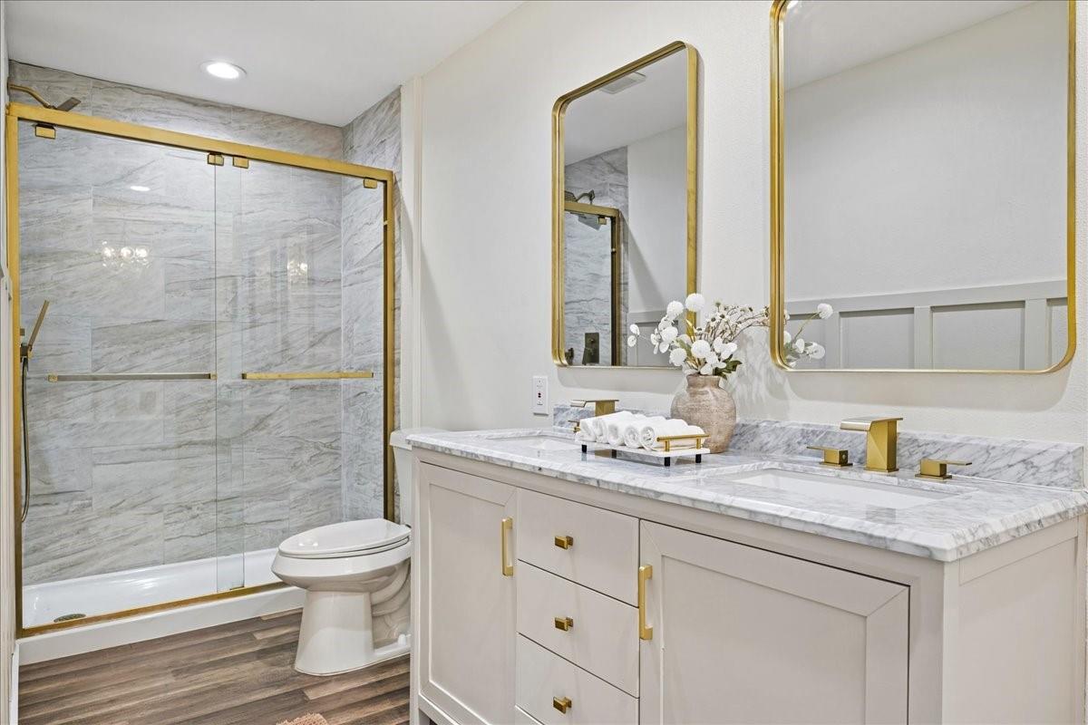 Bathroom with a marble-look shower, glass doors, and white vanity with gold fixtures.