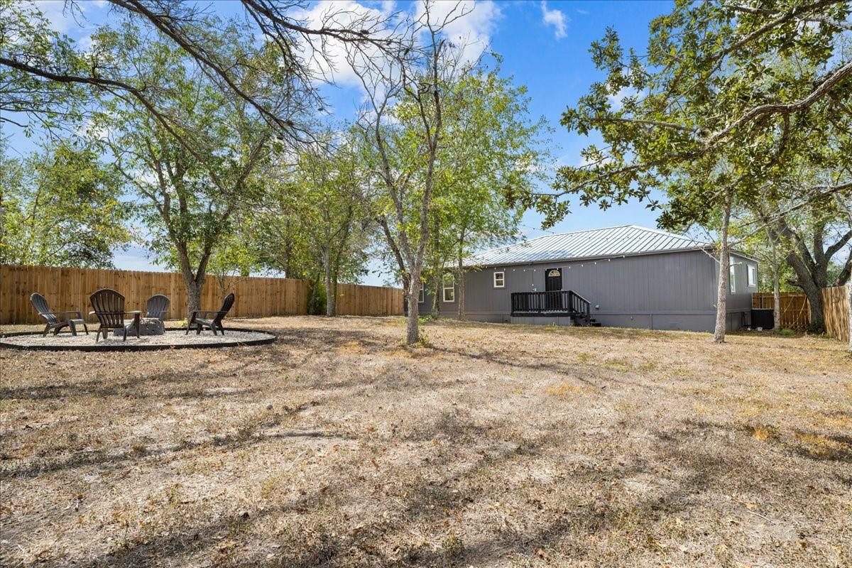 Gray home with a metal roof and raised entry deck in a fenced, tree-shaded yard.