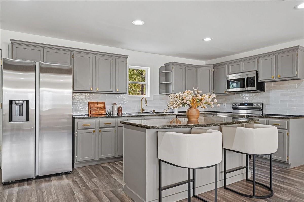 Staged kitchen with gray cabinets, stainless steel appliances, and a large island with two white stools.