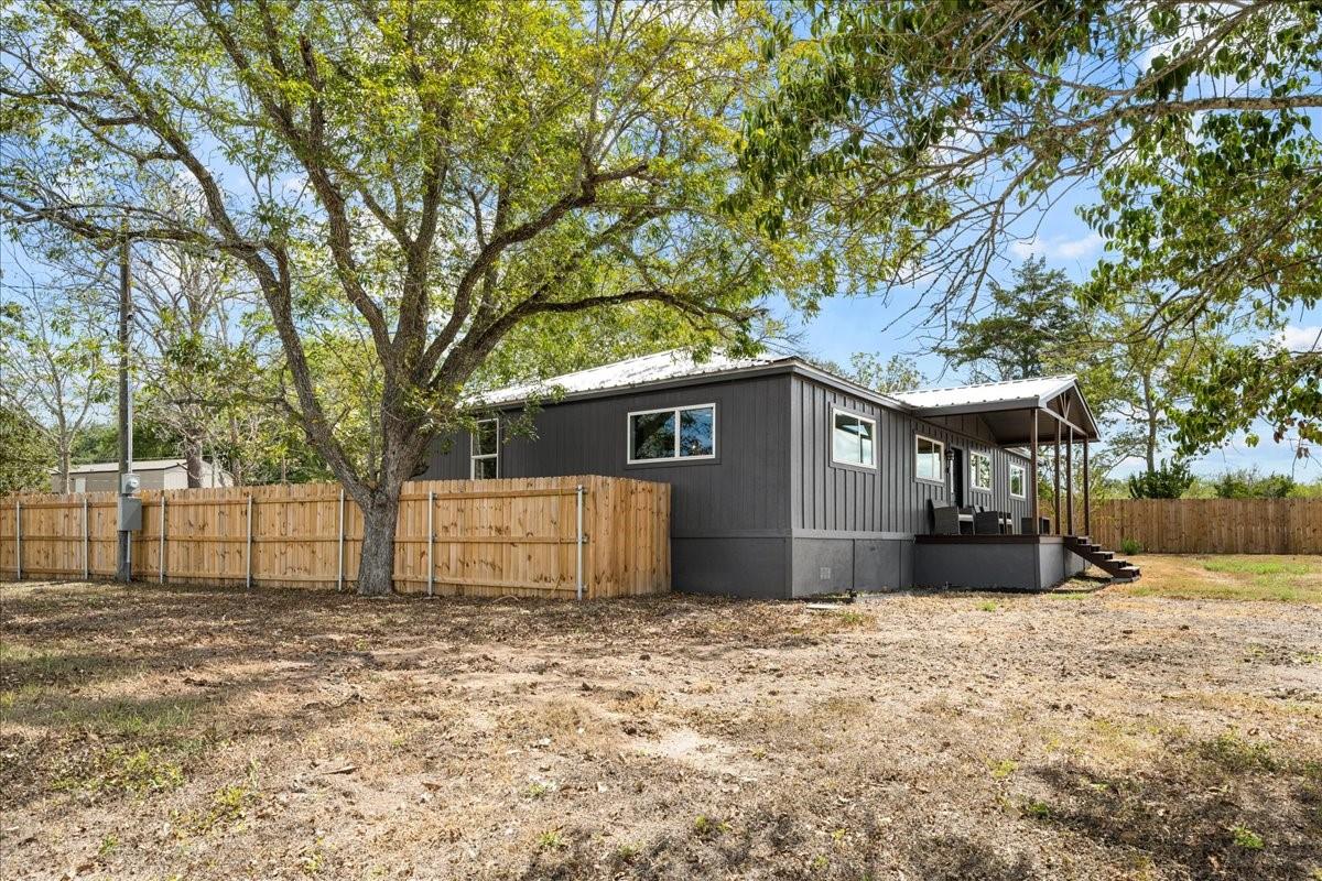 Dark gray single-story home with a covered porch, wooden privacy fence, and large shade tree.
