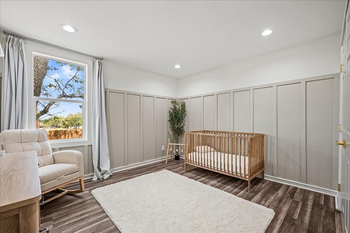 Furnished nursery with a wooden crib, cream rocking chair, gray paneled walls, and a large curtained window.