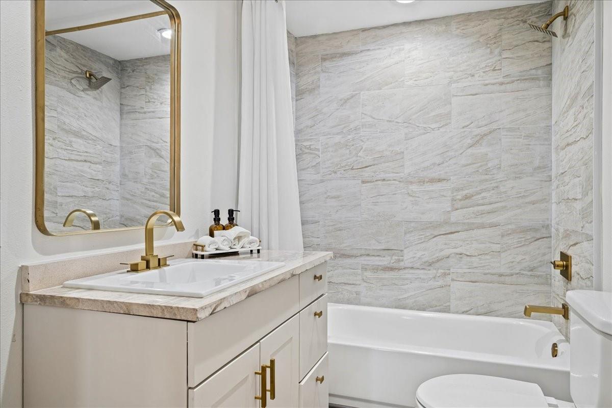 Bathroom with a marble-look tub surround, white vanity, and gold-tone fixtures.