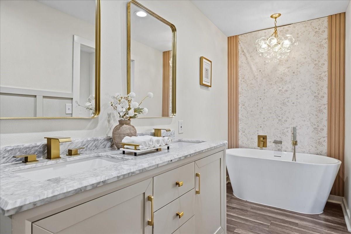 Bathroom with a marble-look double vanity and brass fixtures beside a freestanding tub.
