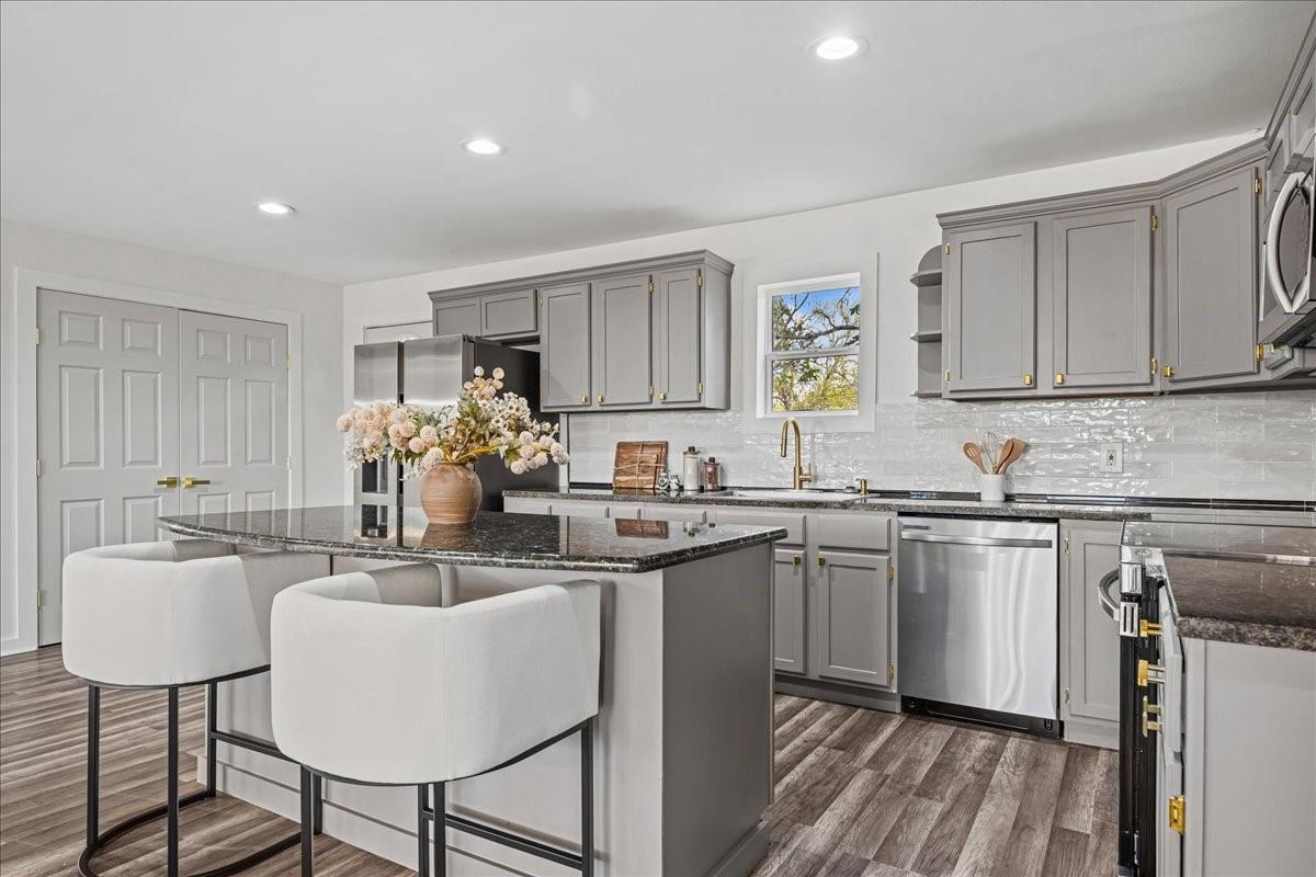 Kitchen with gray cabinets, stainless steel appliances, and a dark stone island with two white barstools.