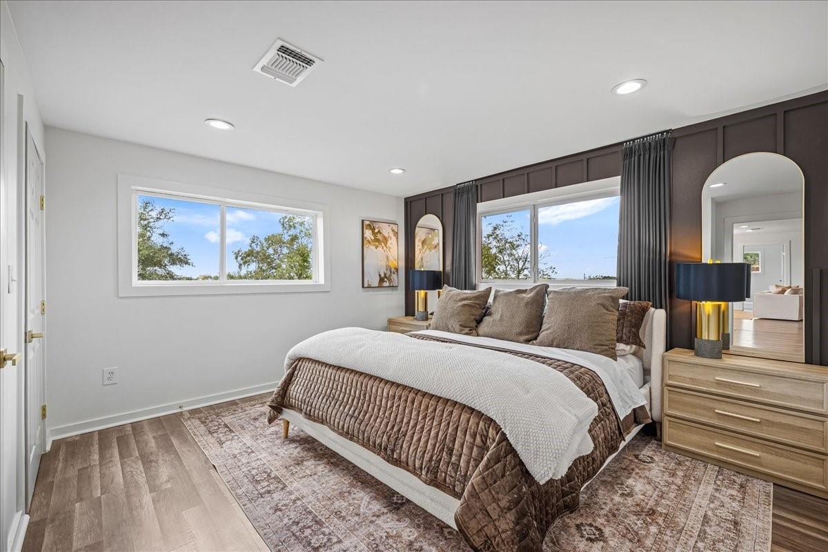 Staged bedroom with a large bed, dark paneled accent wall, and two windows.
