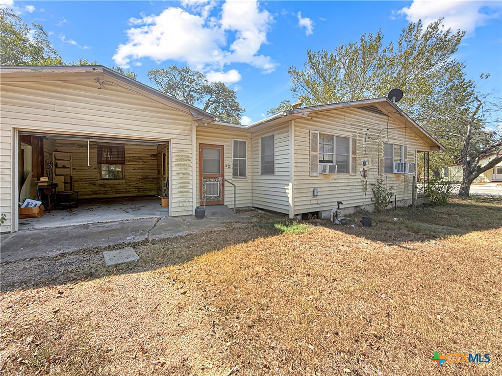 Single-story house with an open garage, covered entry, and dry leaf-covered yard.