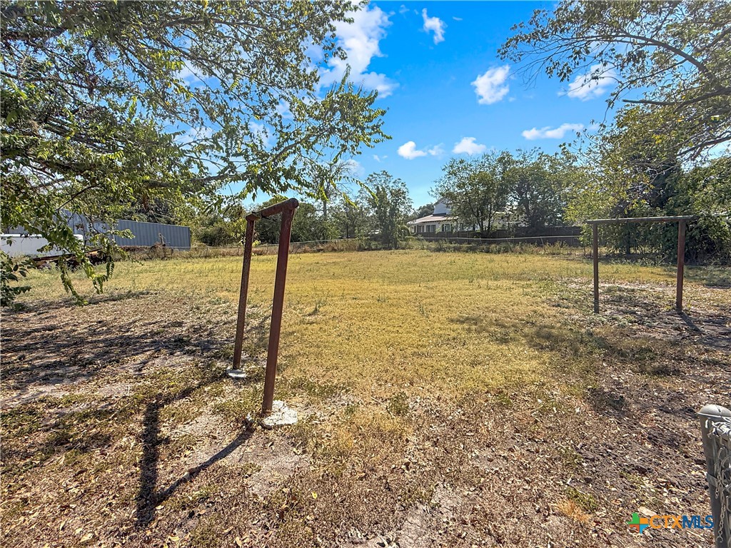 Fenced backyard with dry grass, mature trees, and clothesline posts.
