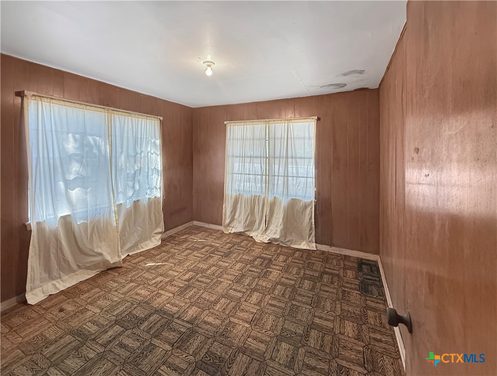 Vacant room with brown paneled walls, patterned carpet, and two curtained windows.