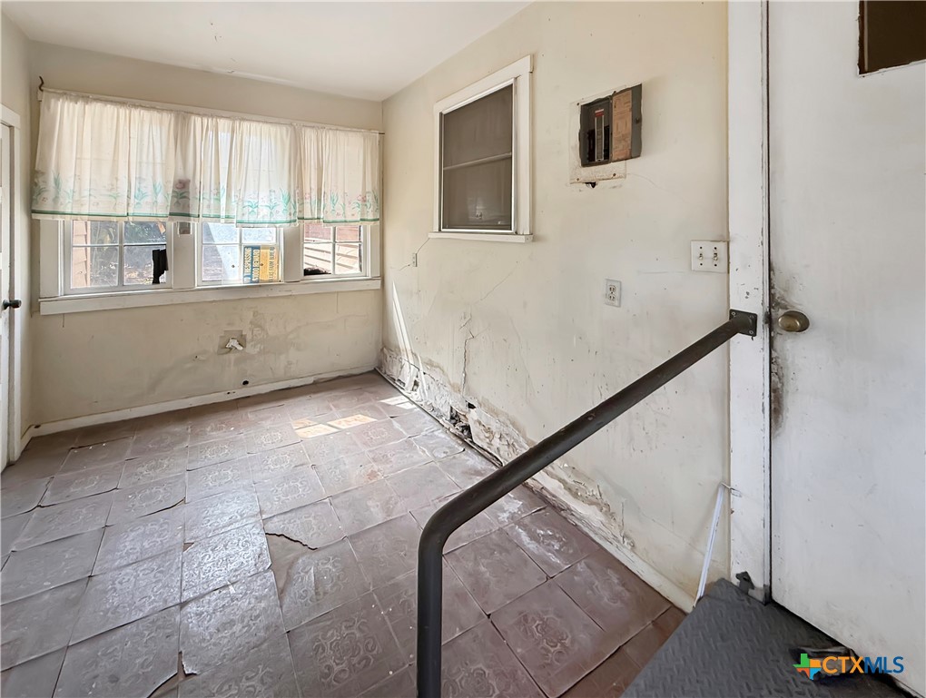 Vacant room with patterned tile floors, curtained windows, damaged walls, and a metal handrail.