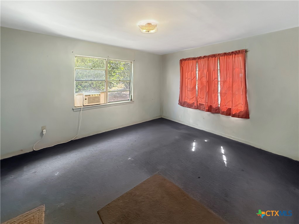 Empty room with dark flooring, a window air conditioner, and red curtains.