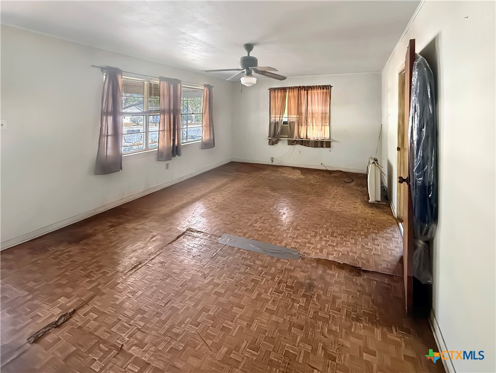 Empty room with parquet flooring, curtained windows, and a ceiling fan.