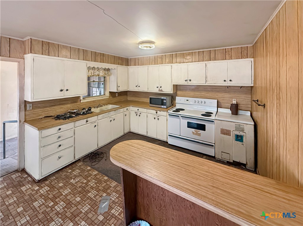 Kitchen with white cabinets, wood-look counters, an electric range, and a broad peninsula.