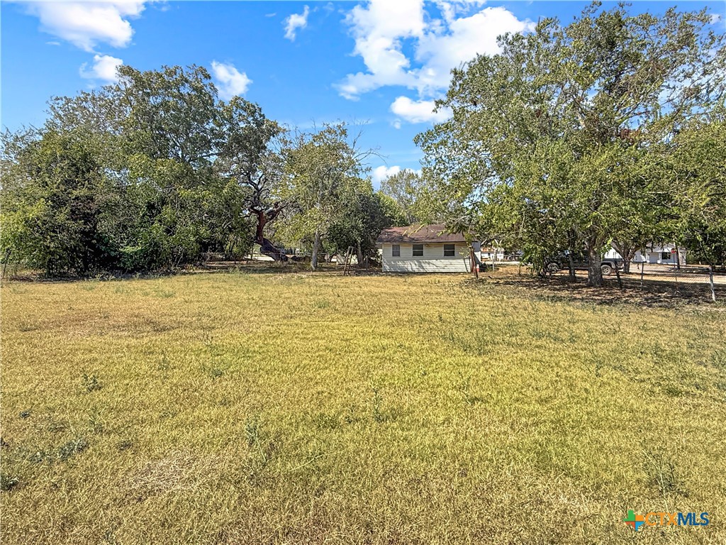 Grassy property lot with mature trees and a small house in the distance.