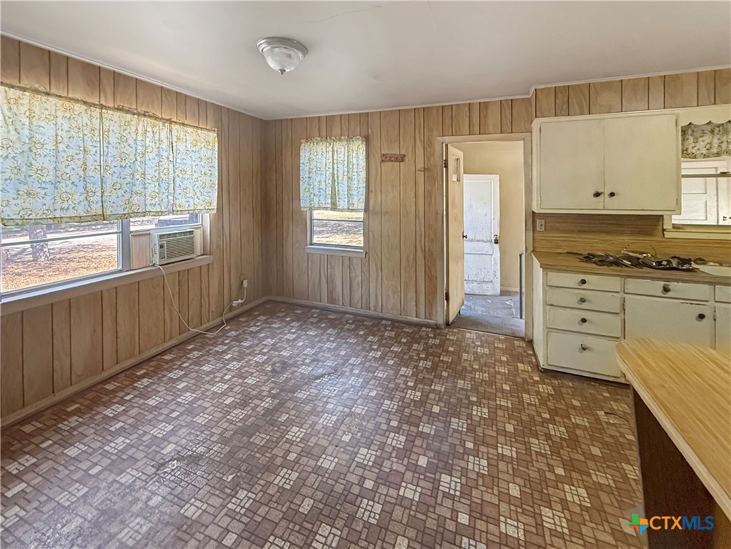 Vacant kitchen with wood paneling, patterned flooring, floral shades, and cream cabinets.