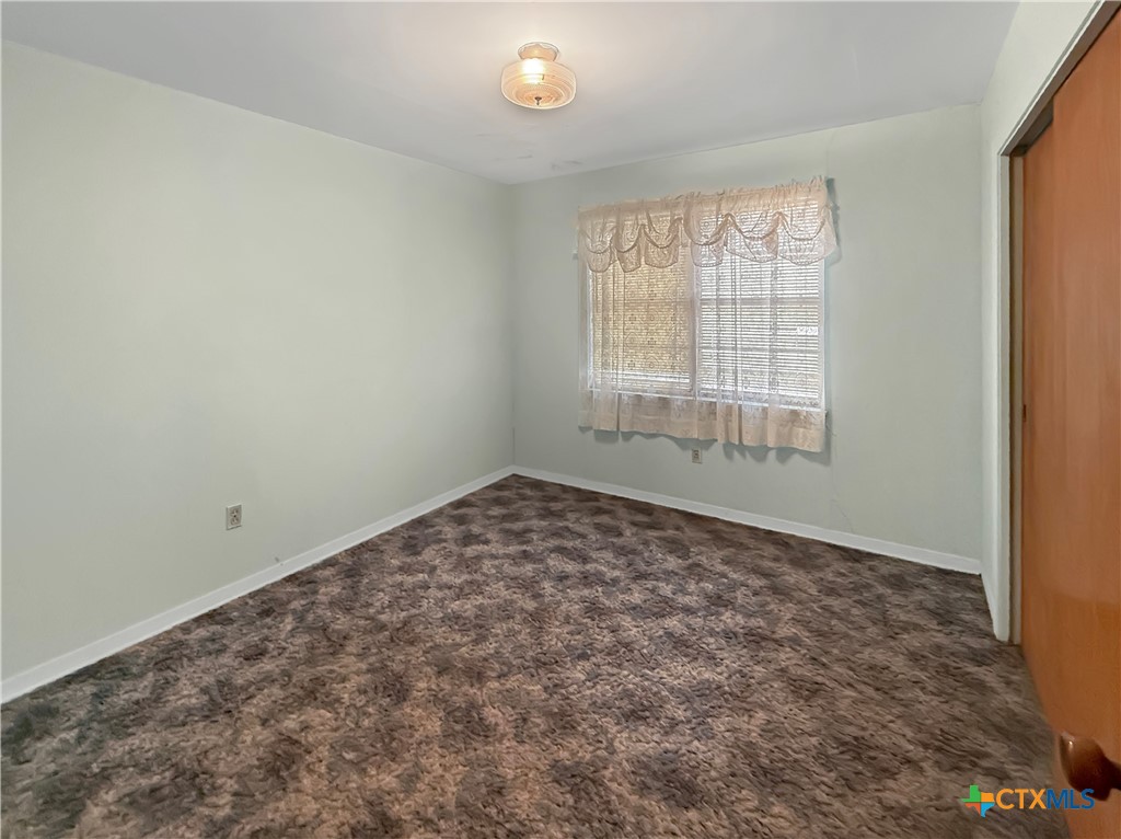 Empty carpeted room with a curtained window, blinds, and a ceiling light.
