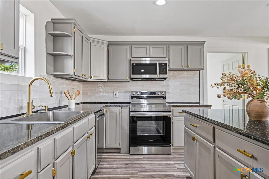 Updated kitchen with gray cabinets, dark countertops, stainless steel appliances, and a flower arrangement on the island.