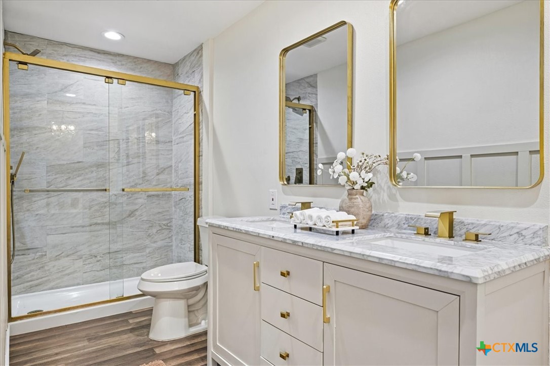 Bathroom with a marble-look glass shower and white vanity, accented by gold fixtures and mirrors.