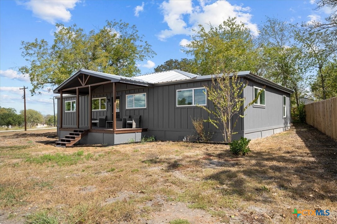 Single-story gray home with a covered porch, metal roof, and dry yard.