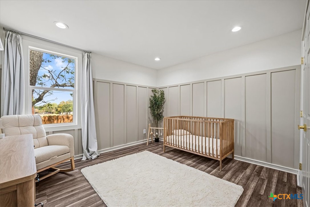 Staged nursery with a wooden crib, paneled walls, and a large window beside an upholstered armchair.