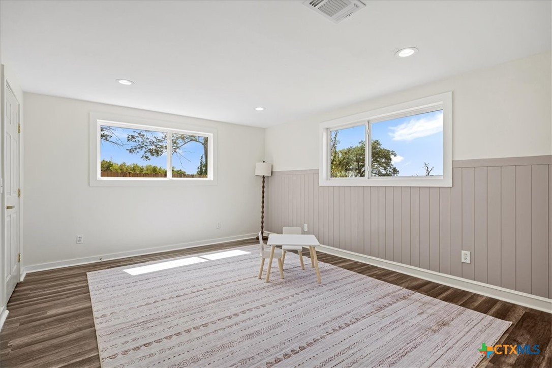 Bright, sparsely staged room with paneled wainscoting, two windows, and a large patterned rug.