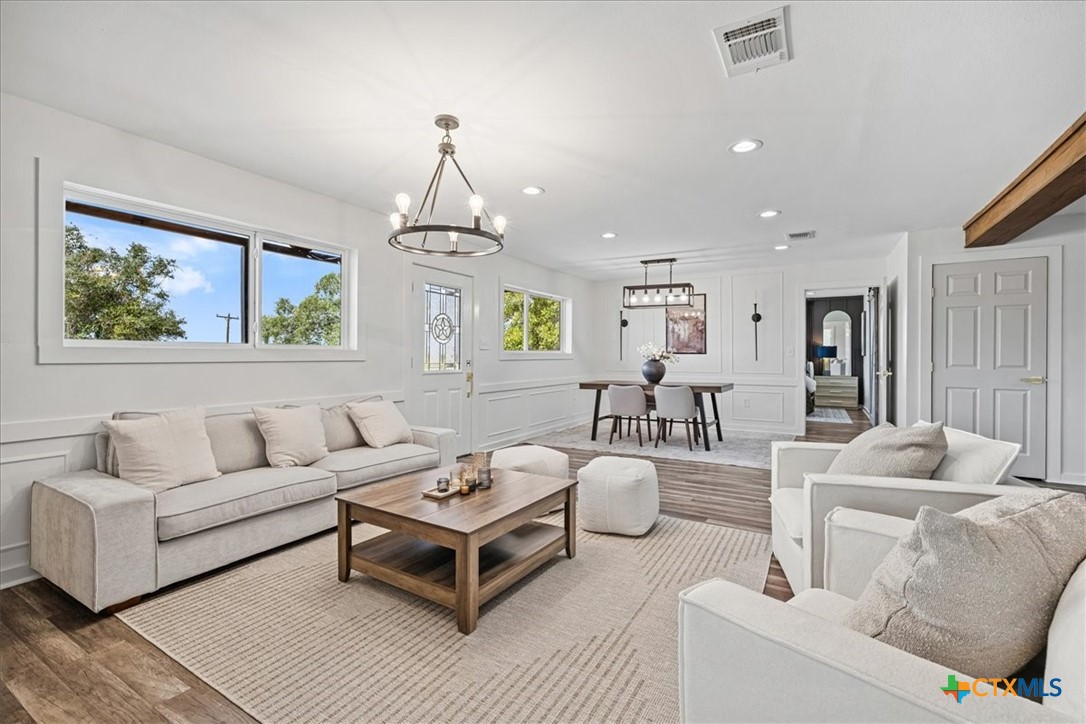 Staged living room with a dining area, large windows, neutral furnishings, and wood-look floors.