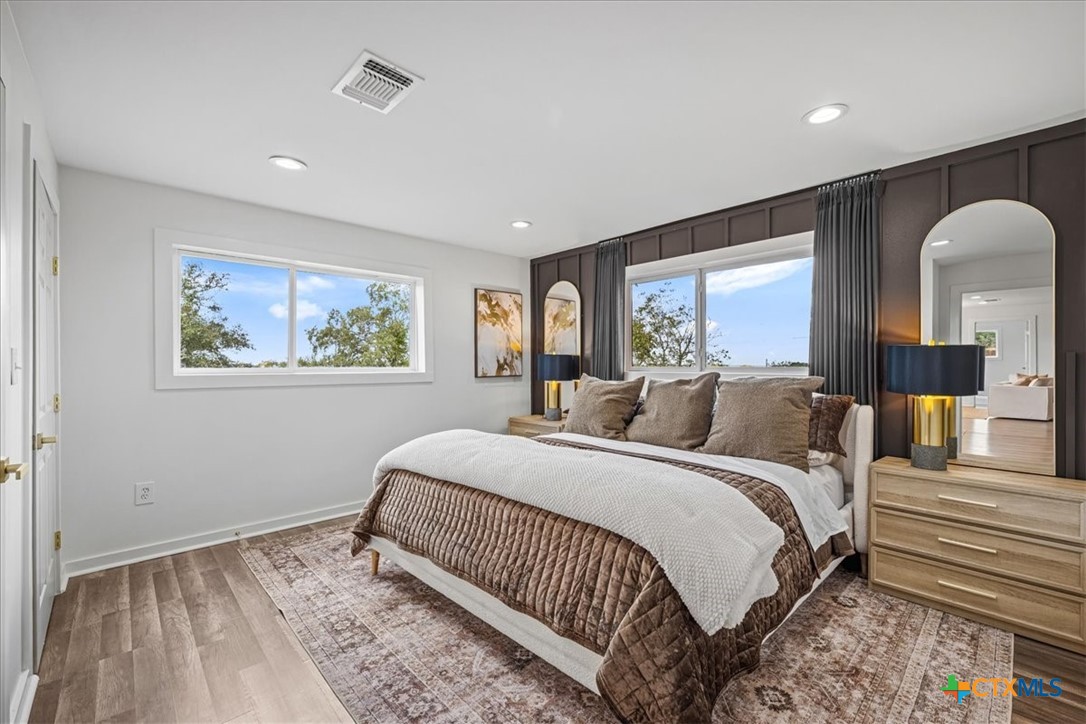 Staged bedroom with a large bed, dark paneled accent wall, and windows overlooking trees.