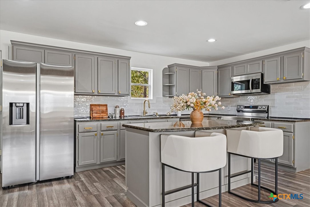 Remodeled kitchen with gray cabinets, stainless steel appliances, and a large island with two white stools.